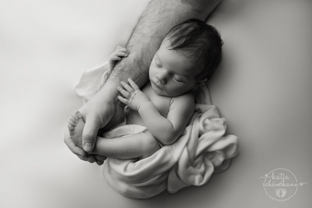 Neugeborenes Baby umklammert den Arm seines Vaters